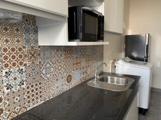 Modern kitchen with patterned tile backsplash, black countertop, and appliances