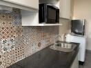 Modern kitchen with patterned tile backsplash, black countertop, and appliances