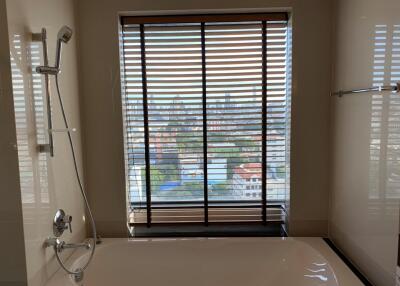 Bathroom with bathtub and city view through blinds