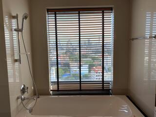 Bathroom with bathtub and city view through blinds