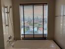 Bathroom with bathtub and city view through blinds