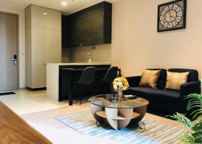 Modern living room and kitchen with black sofa, glass coffee table, and wall clock