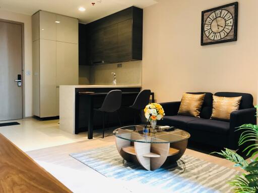 Modern living room and kitchen with black sofa, glass coffee table, and wall clock