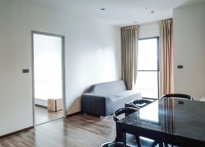 Modern living room with gray sofa, dining area, and view of bedroom