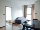 Modern living room with gray sofa, dining area, and view of bedroom