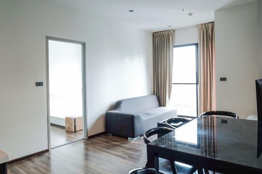 Modern living room with gray sofa, dining area, and view of bedroom