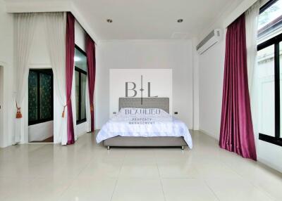 Spacious bedroom with large windows, curtains, and an elegant bed