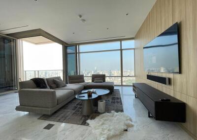 Modern living room with a large sofa, floor-to-ceiling windows with city views, and a mounted TV