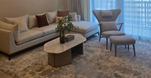 Cozy living room with a sectional sofa, accent chair, stone coffee table, and a large window with sheer curtains