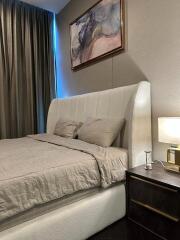 A cozy bedroom with a large bed, nightstand, lamp, and modern decor.