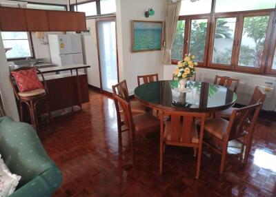 Dining area with round table, six chairs, green sofa, and kitchen in the background