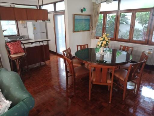 Dining area with round table, six chairs, green sofa, and kitchen in the background