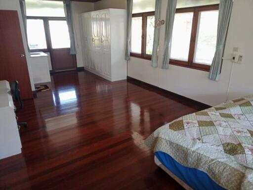 Spacious bedroom with wooden flooring, large windows, and built-in wardrobe