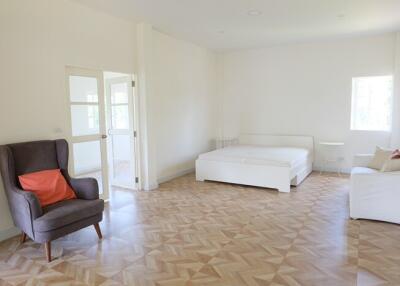 Spacious bedroom with bed, armchair, and natural light