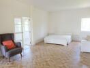 Spacious bedroom with bed, armchair, and natural light