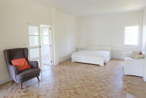 Spacious bedroom with bed, armchair, and natural light