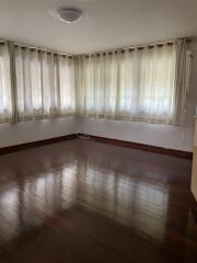 Empty living room with wooden flooring and large windows with curtains