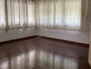 Empty living room with wooden flooring and large windows with curtains