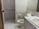 Bathroom with tiled walls and floor, a sink, toilet, and a vanity area.