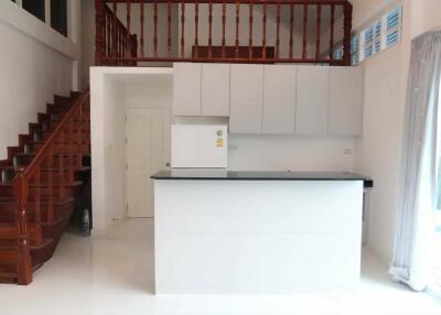 Modern kitchen with white cabinets and black countertop, featuring a wooden staircase and a mezzanine level.