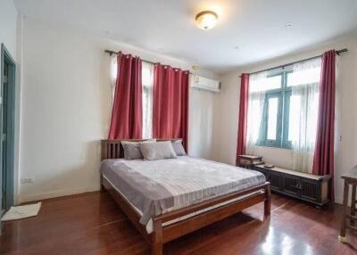 A bedroom with a bed, red curtains, wooden floor, and air conditioning.