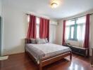 A bedroom with a bed, red curtains, wooden floor, and air conditioning.