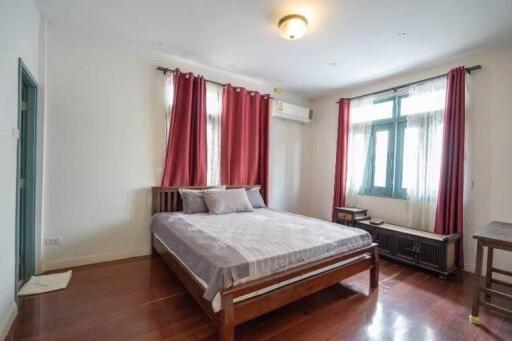 A bedroom with a bed, red curtains, wooden floor, and air conditioning.