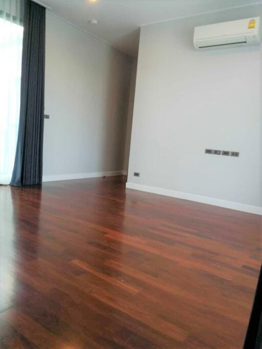 Empty living room with wooden floor, air conditioner, and large window with curtains