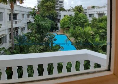 View from a window overlooking a swimming pool and lush greenery in between multiple white buildings