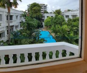 View from a window overlooking a swimming pool and lush greenery in between multiple white buildings