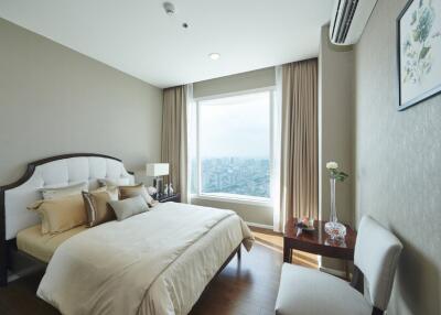 Modern bedroom with a large window offering city views, furnished with a bed, nightstand with lamp, chair and wall art.