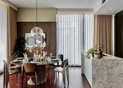 Modern dining room with round table, decorative lighting, and large windows with sheer curtains