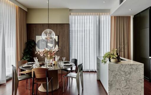 Modern dining room with round table, decorative lighting, and large windows with sheer curtains