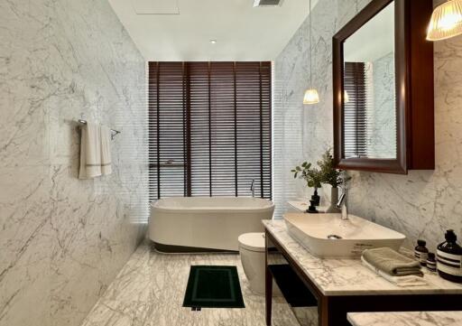 Modern bathroom with marble walls and floor, featuring a freestanding bathtub and stylish sink area