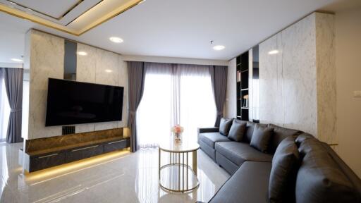 Modern living room with large TV, sectional sofa, and floor-to-ceiling windows