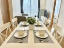 White-themed dining room with table set for four, featuring a centerpiece, and overlooking a modern living space with TV.