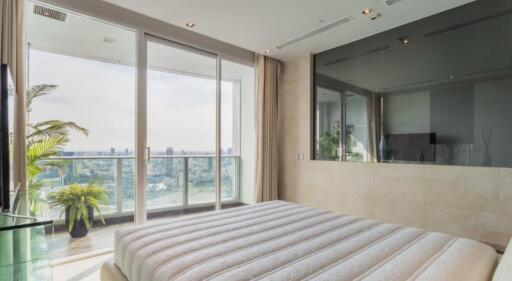 Spacious bedroom with a large bed and floor-to-ceiling windows leading to a balcony with a city view