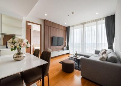 Modern living room with a large window, comfortable gray sofa, wall-mounted TV, wooden floor, and dining area.