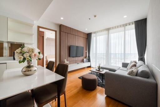 Modern living room with a large window, comfortable gray sofa, wall-mounted TV, wooden floor, and dining area.