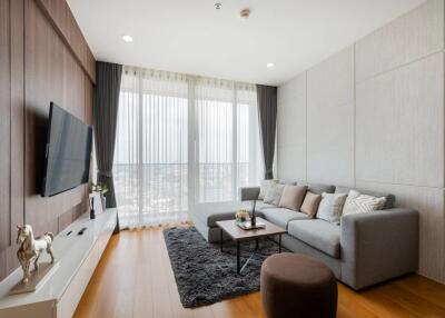 Modern living room with a large grey sofa, TV, and floor-to-ceiling windows