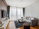 Modern living room with a large grey sofa, TV, and floor-to-ceiling windows