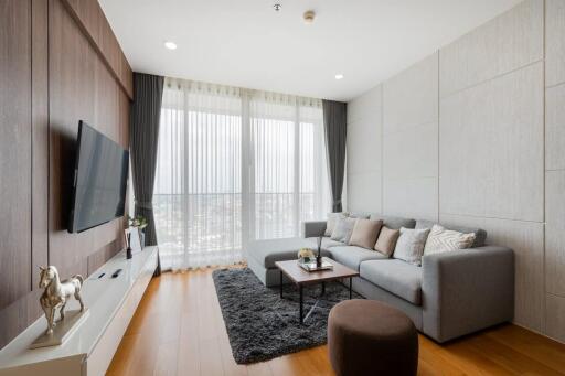 Modern living room with a large grey sofa, TV, and floor-to-ceiling windows