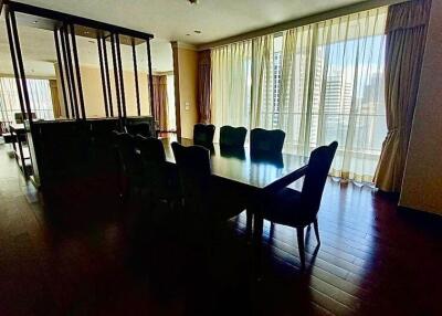 Spacious dining area with a large table and chairs, adjacent to a living room with large windows.