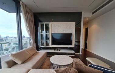 Modern living room with large windows, beige couches, a marble coffee table, and a TV