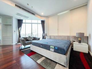 Modern bedroom with large bed, seating area, and city view