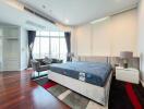 Modern bedroom with large bed, seating area, and city view