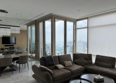 Modern living room with large windows, a grey sectional sofa, dining area, and city skyline view