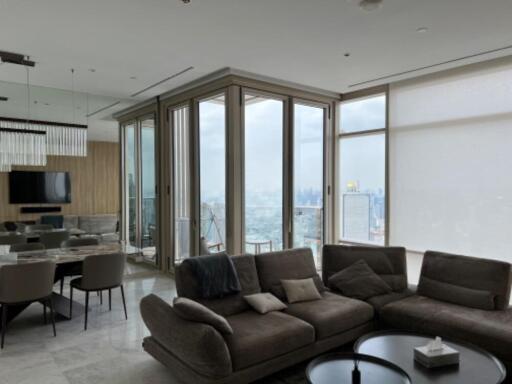 Modern living room with large windows, a grey sectional sofa, dining area, and city skyline view