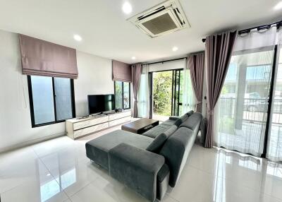 Modern living room with a sectional sofa, TV, and large windows with curtains