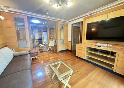 Modern living room with wooden flooring, a large sofa, a flat-screen TV, and a glass coffee table